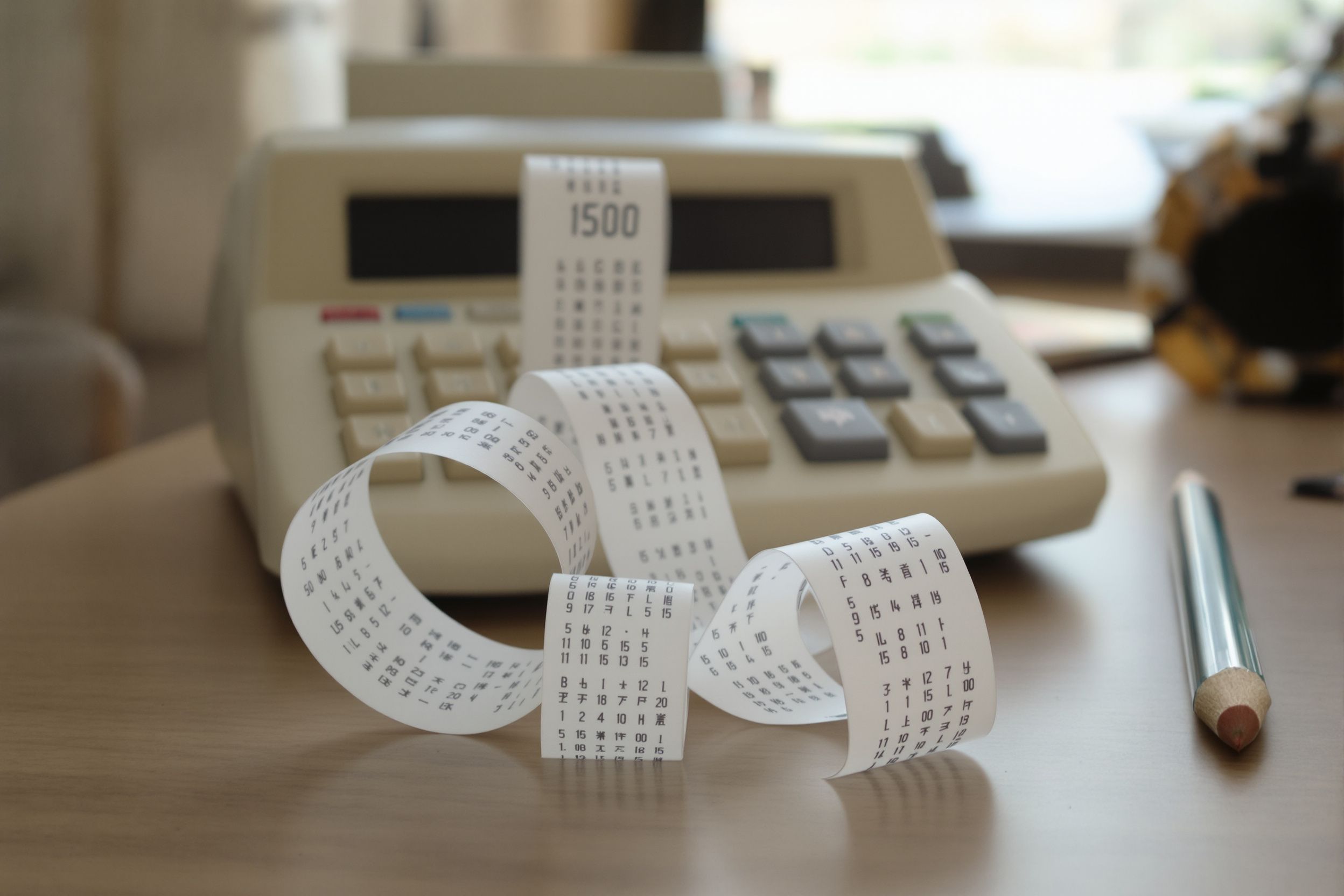 A printing calculator with a long curl of paper tape across a desk